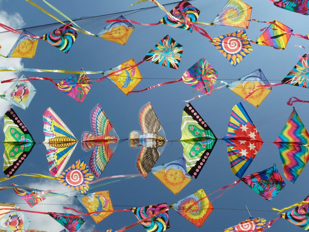 A collection of brightly colored kites strung together to create a canopy against a blue sky.