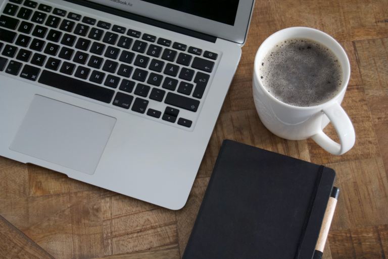 Best sites to hire Java developers | Laptop computer on a desk with a cup of coffee and a notebook on the right side.