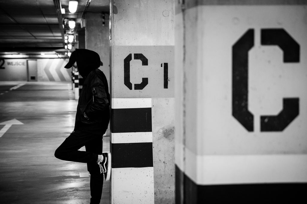 Best sites to hire C# developers | Black and white image of a person wearing a hat, hoodie, jeans, and Vans Old Skools leaning up against a cement beam with the letter C on the side.