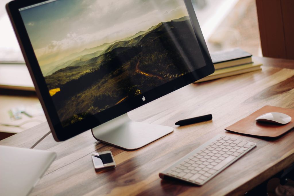 Vue JS developer job description | Mac desktop on a wooden desk with an Apple keyboard and magic mouse.
