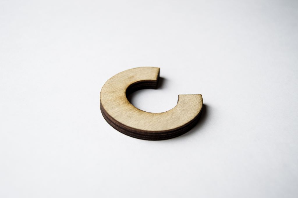 C# junior developer interview questions | A wooden letter C against a white background, shot at an angle from the lower right corner of the letter.
