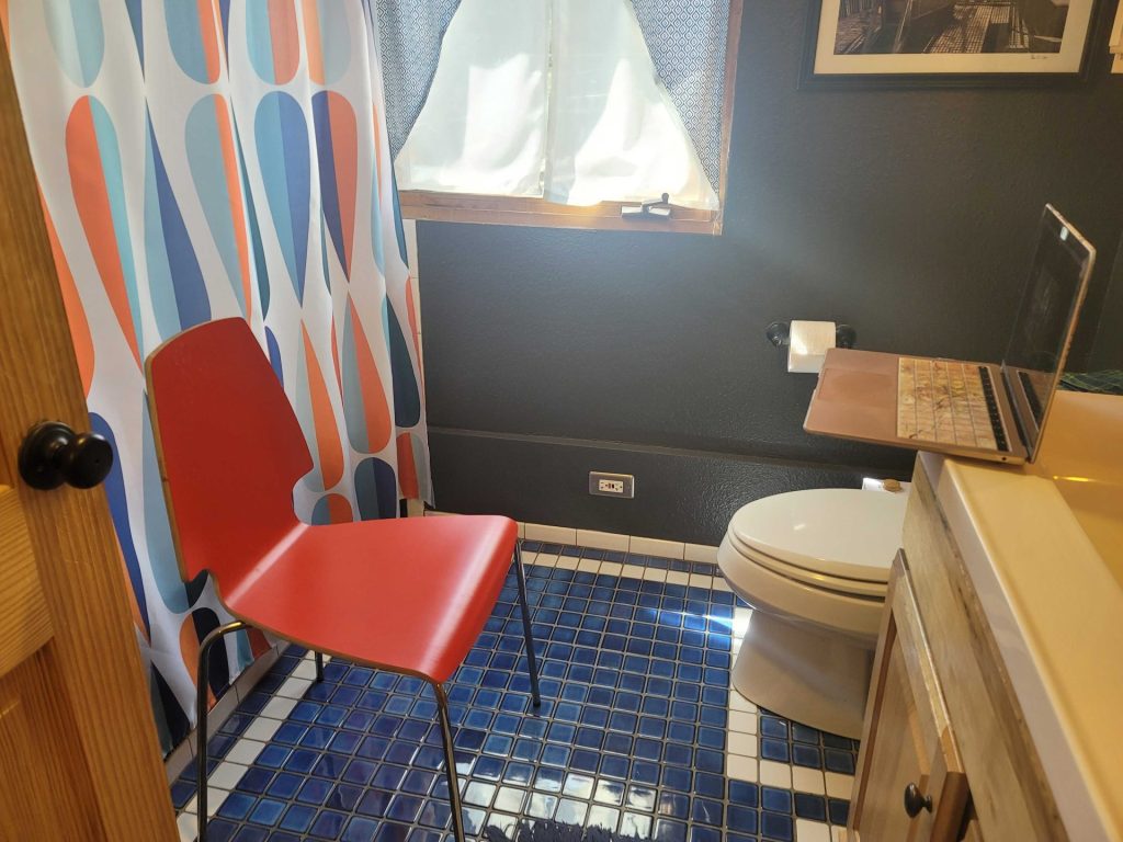 Photo of a chair in front of a shower curtain in a bathroom, facing an open laptop on the bathroom counter