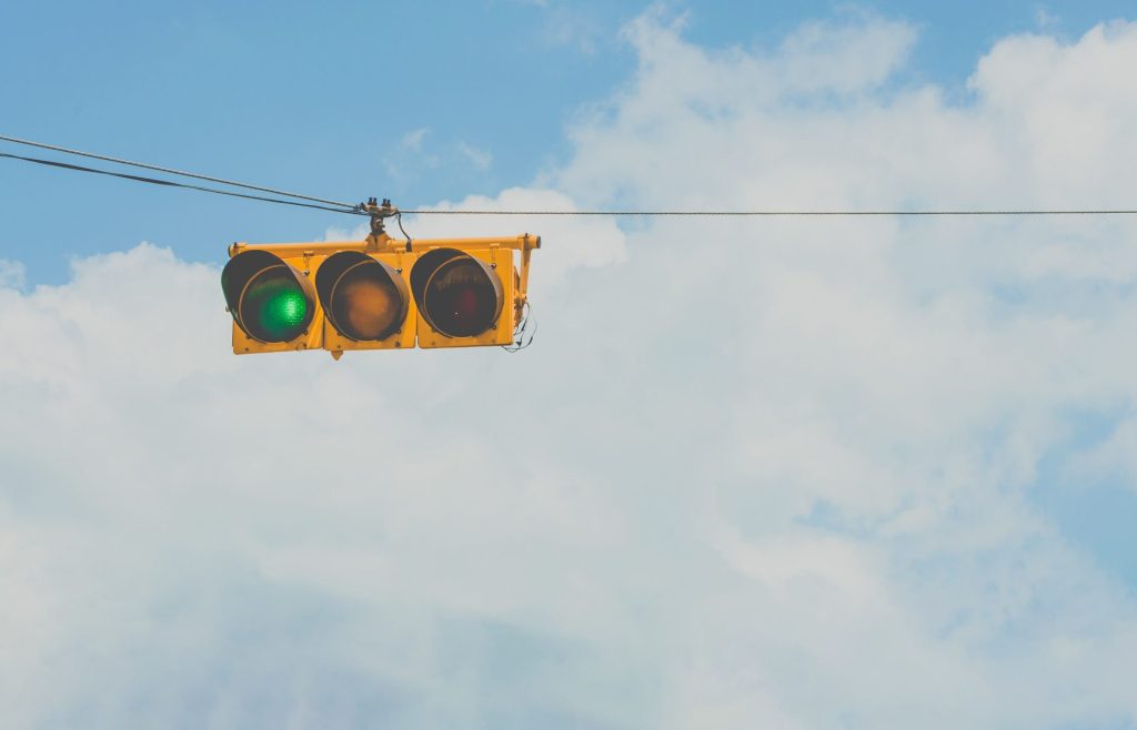 Golang engineer job description | Yellow stoplight, hung horizontally. The green light is lit and in the background is a blanket of clouds with blue sky in the upper right corner.
