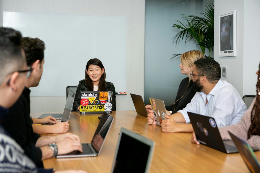 Group of people sitting around a conference table with open laptops.