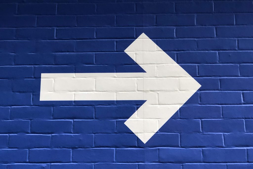 Best sites to hire Next.js developers | Background is a brick wall painted royal blue, with a white arrow pointing to the right.