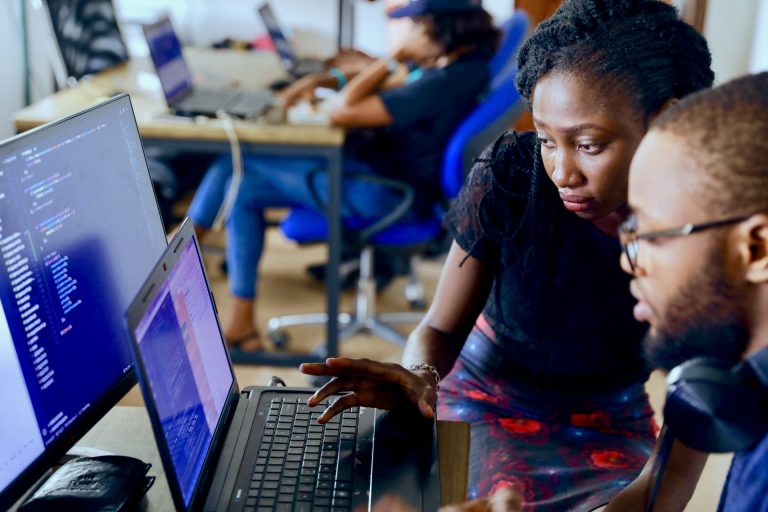Find freelance software developers | Close-up of two people looking at a computer screen with code, inside of a busy office