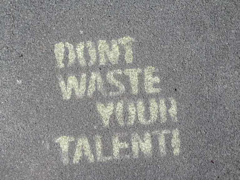 "Don't waste your talent" spray painted as a stencil in yellow paint against dark grey asphalt