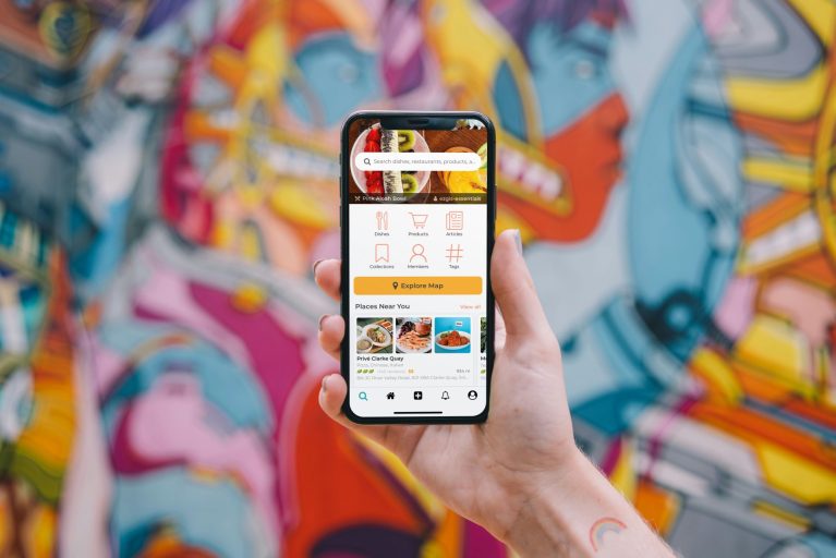 Hire mobile app developers | A hand holding a phone with an app on the screen, against a colorful mural on a wall behind the hand and the phone.